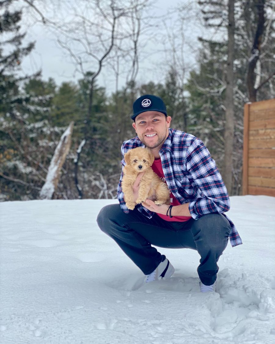 Andrew crouching in the snow holding a goldendoodle puppy